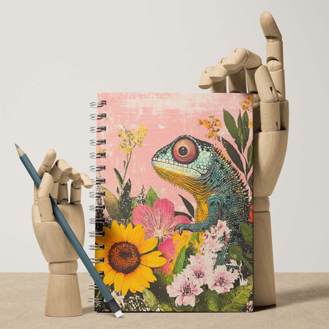 Notebook with a colorful lizard and floral design held by a mechanical arm on a beige background